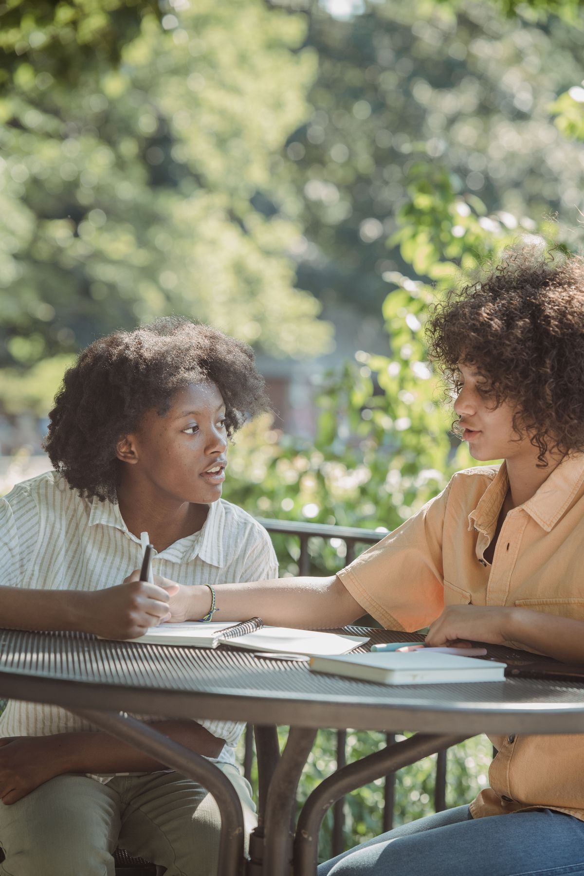 Two teenagers talking and taking notes together at an outdoor table.