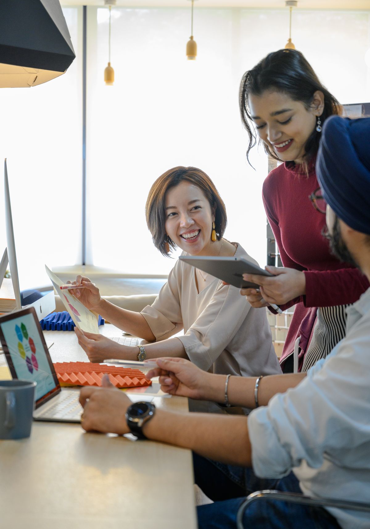 A small, diverse team collaborating around a laptop in a bright office.