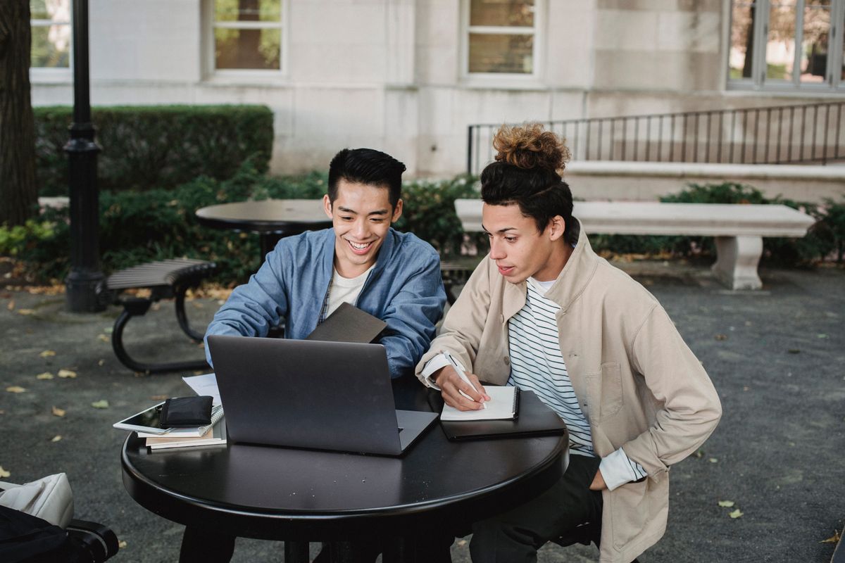 Two students working together with a laptop and notes on a university campus.