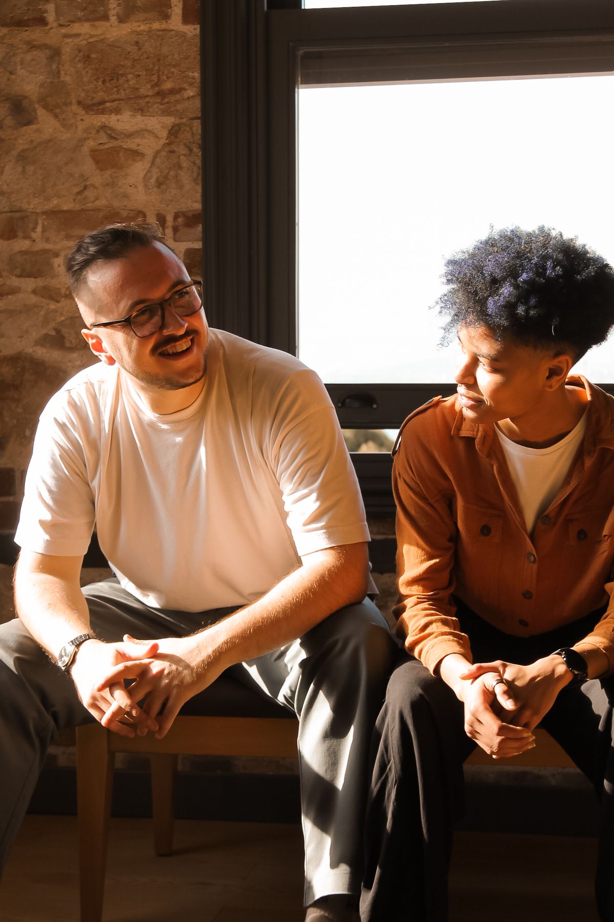 Two young people in a warm one-on-one conversation by a window.