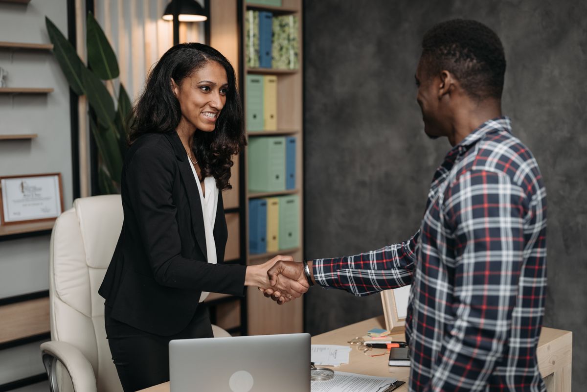 Two professionals shaking hands across a desk in a bright office.